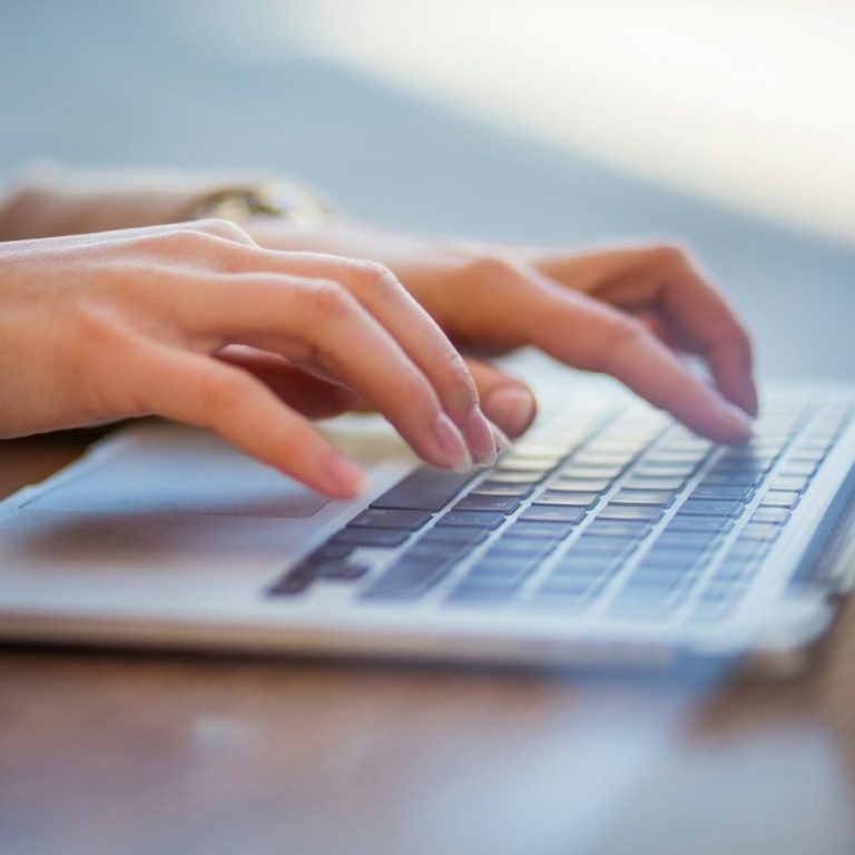 Hände tippen auf einer Laptop-Tastatur auf einem Schreibtisch – Symbol für Schreibservice und Transkription.